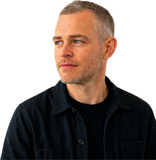 Tom Sharp, wearing a dark overshirt over a black t-shirt, turned slightly towards the page.